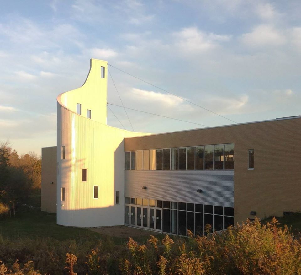 The Centre, home of Centre Fellowship Church, a two-storey building of buff brick and white metal panels with a band of windows and a tall curved white tower at its corner, in evening sun
