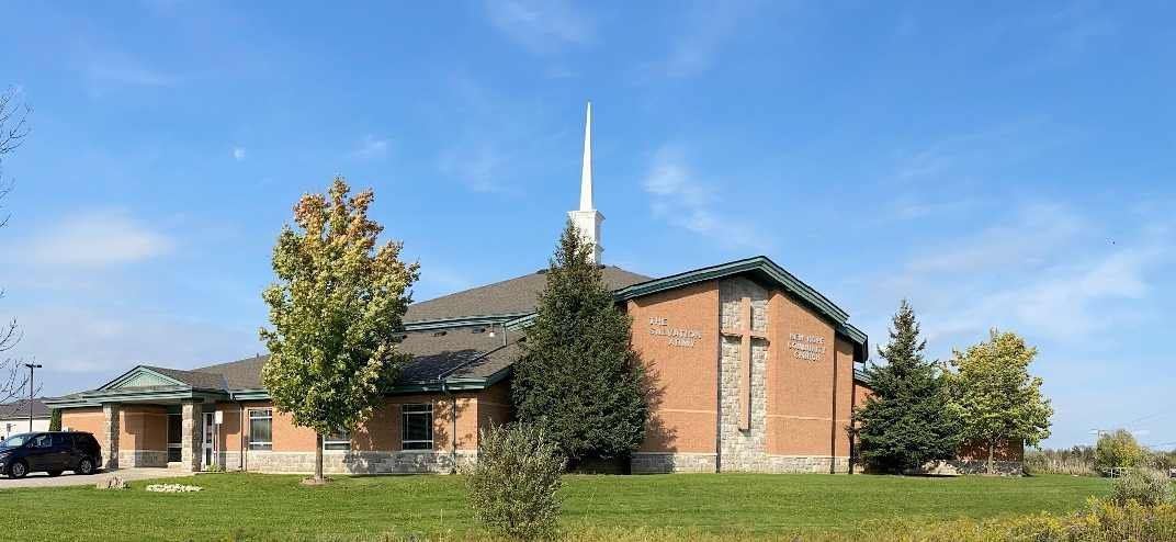 The Salvation Army New Hope Community Church, a long single-storey brick church with a white steeple, a stone-faced gable bearing a tall cross between the Army's name and the church's, and a covered entrance at the left